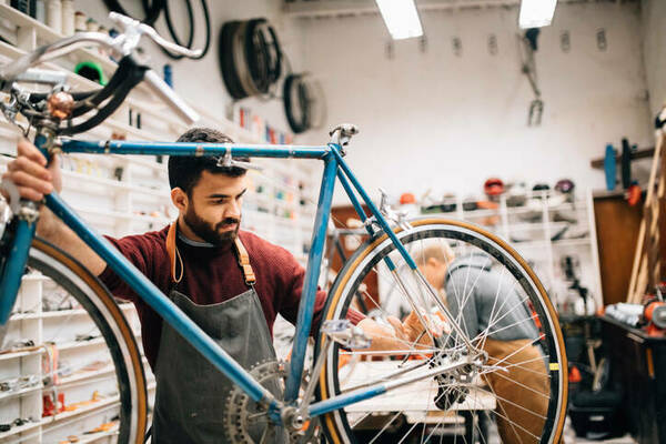 Bearded man in apron working on a bicycle in a bicycle shop who has started a business as a way out of poverty