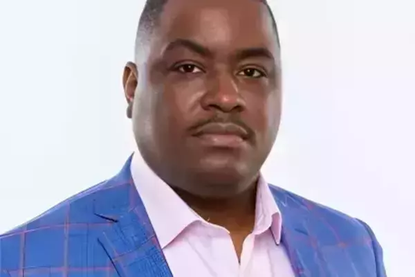 Headshot of man wearing a blue blazer, pink button-down shirt, and red handkerchief against a white background