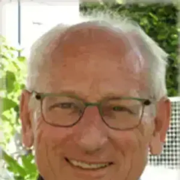Smiling man with white hair, green glasses, and a red and blue plaid shirt.